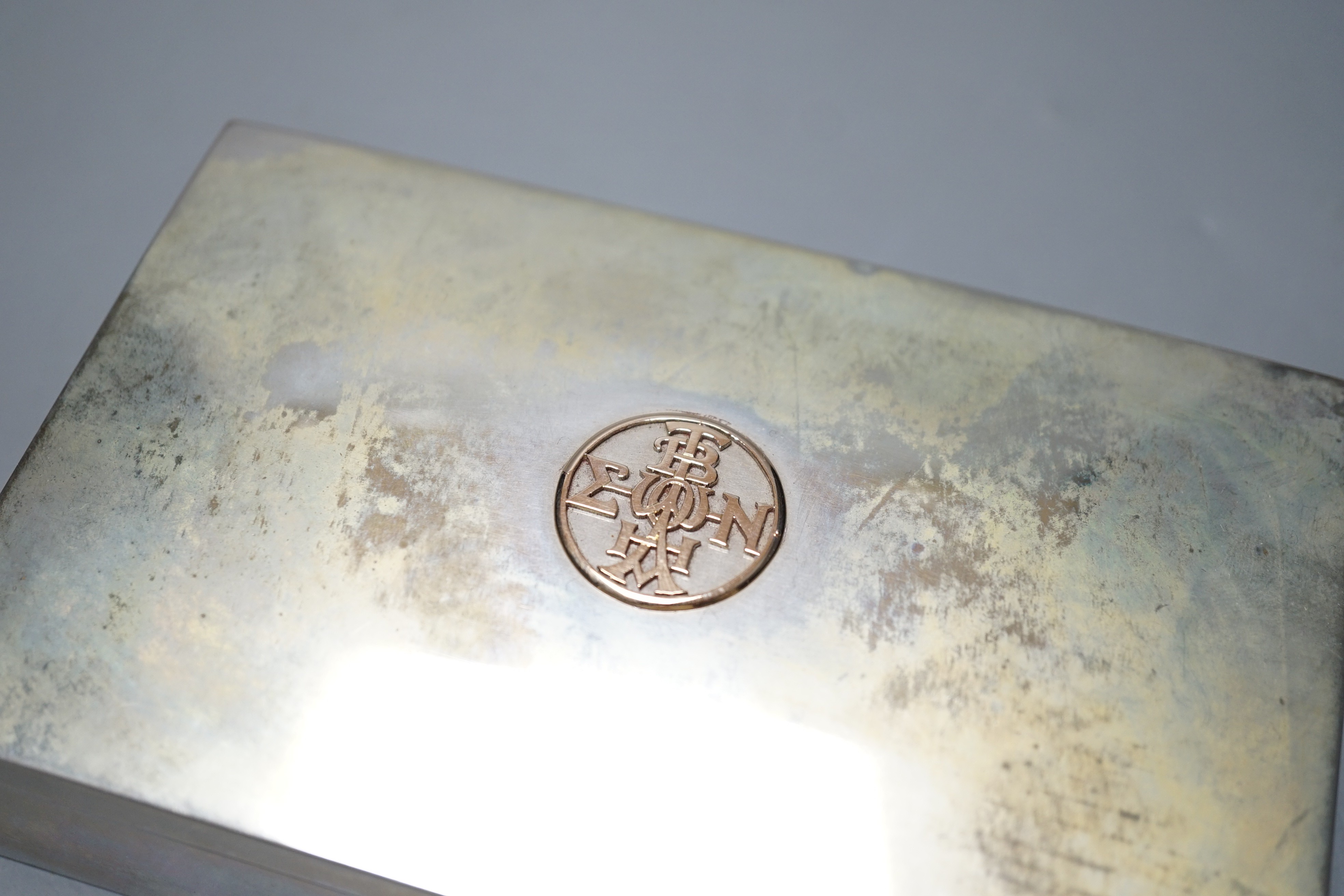 A white metal rectangular cigarette box, with yellow metal appliqué, 15.1cm, gross 15.1oz.